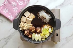 Disposition esthétique des légumes, du tofu et des shirataki par zones thermiques dans la marmite de sukiyaki.