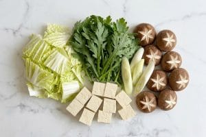 Ingrédients du sukiyaki découpés à cru : tofu, naganegi, champignons shiitake incisés, chou nappa et shungiku.